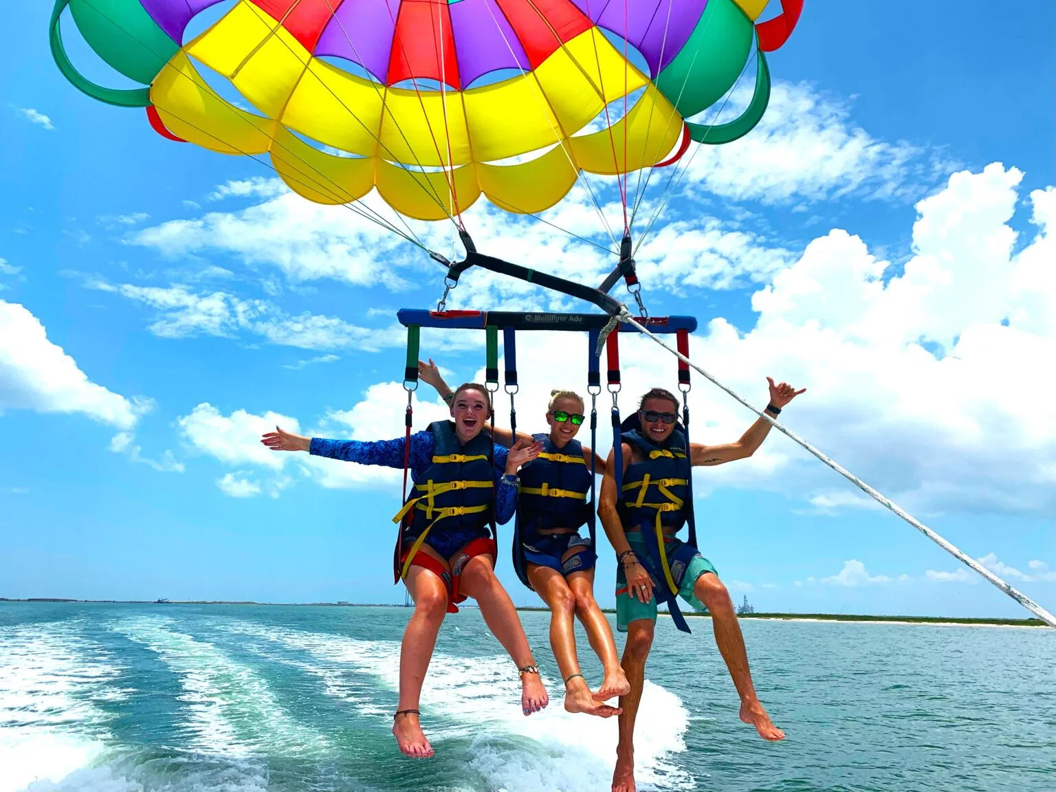 Three individuals enjoy parasailing behind a boat