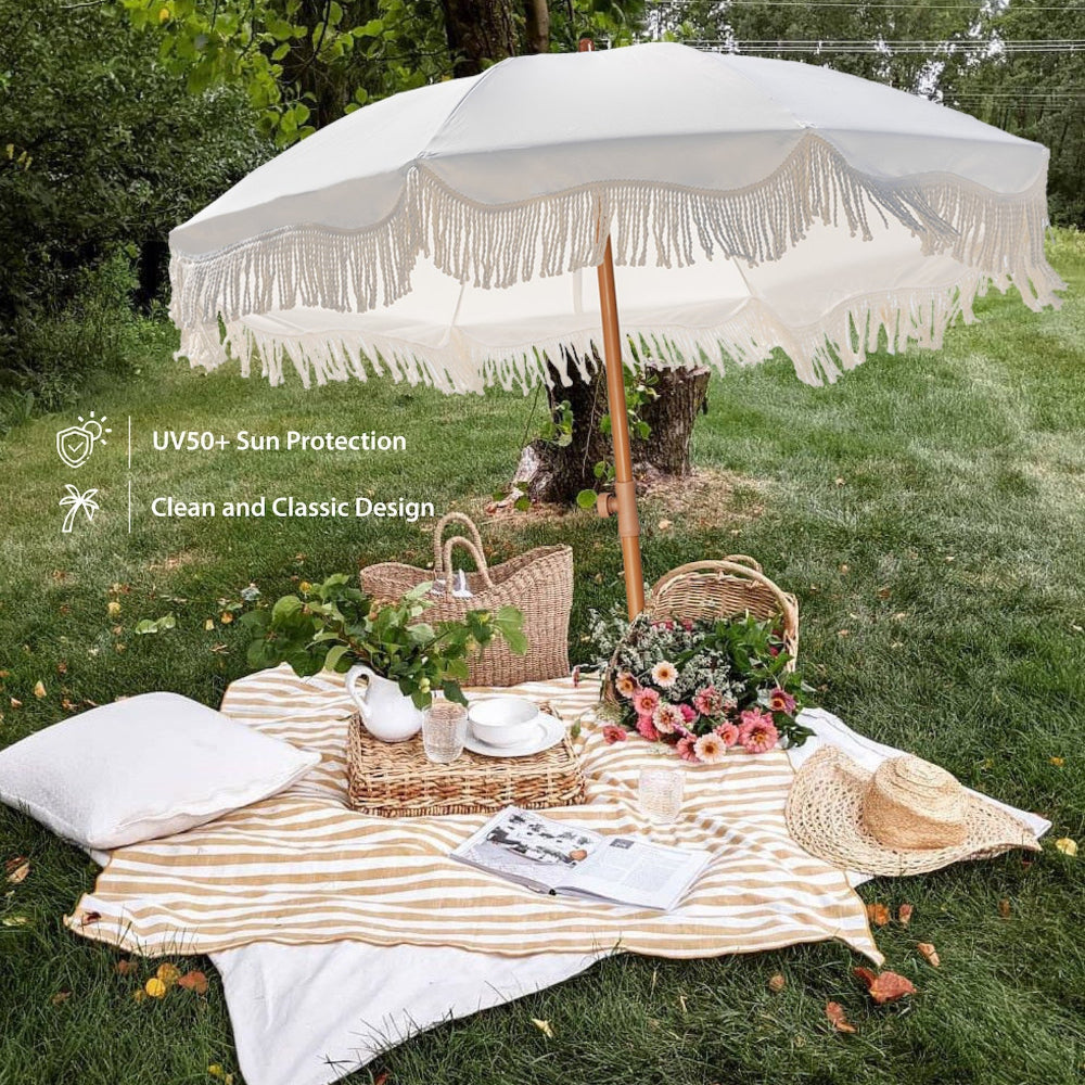 Picnic setup with AMMSUN 6.5ft white beach umbrellas with fringe, tablecloth, plates, and flowers on grass.