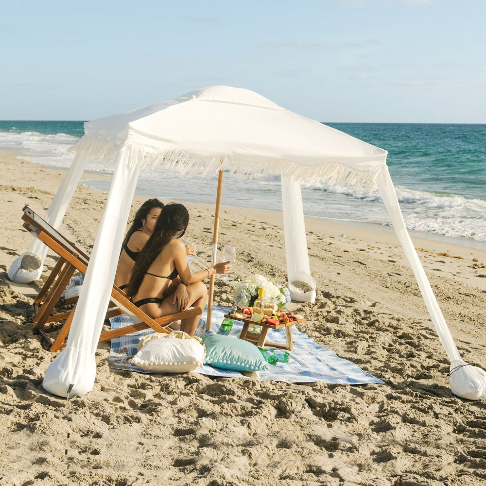 Two women enjoying a sunny day under AMMSUN 6'×6' Bobo Beach cabana umbrella with Fringe,Elegant white treepod cabana with stand
