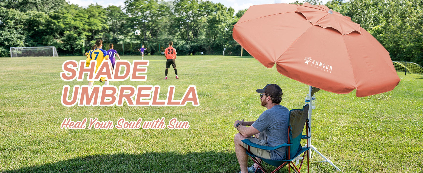 Person sitting under an AMMSUN 6.5ft peach pink sports umbrella portable umbrella with stand for outdoors on the football field.