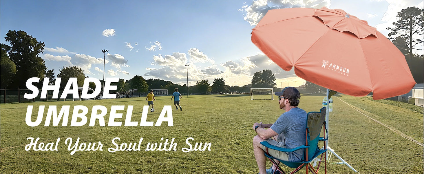 A man sitting under an AMMSUN 6.5ft peach pink sports umbrella portable umbrella with stand on the football field.