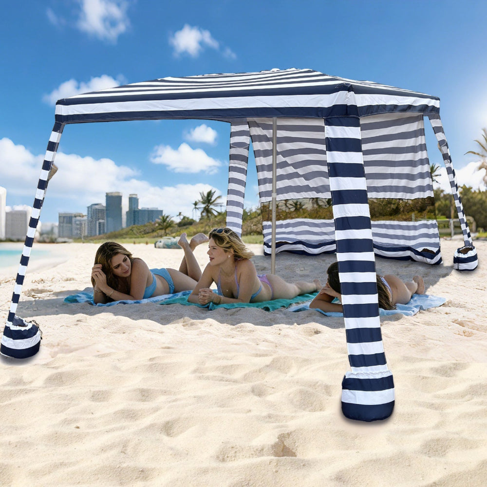 Two women lying under an AMMSUN 8'x8' navy blue stripe folded beach tent sun shelter with privacy wall