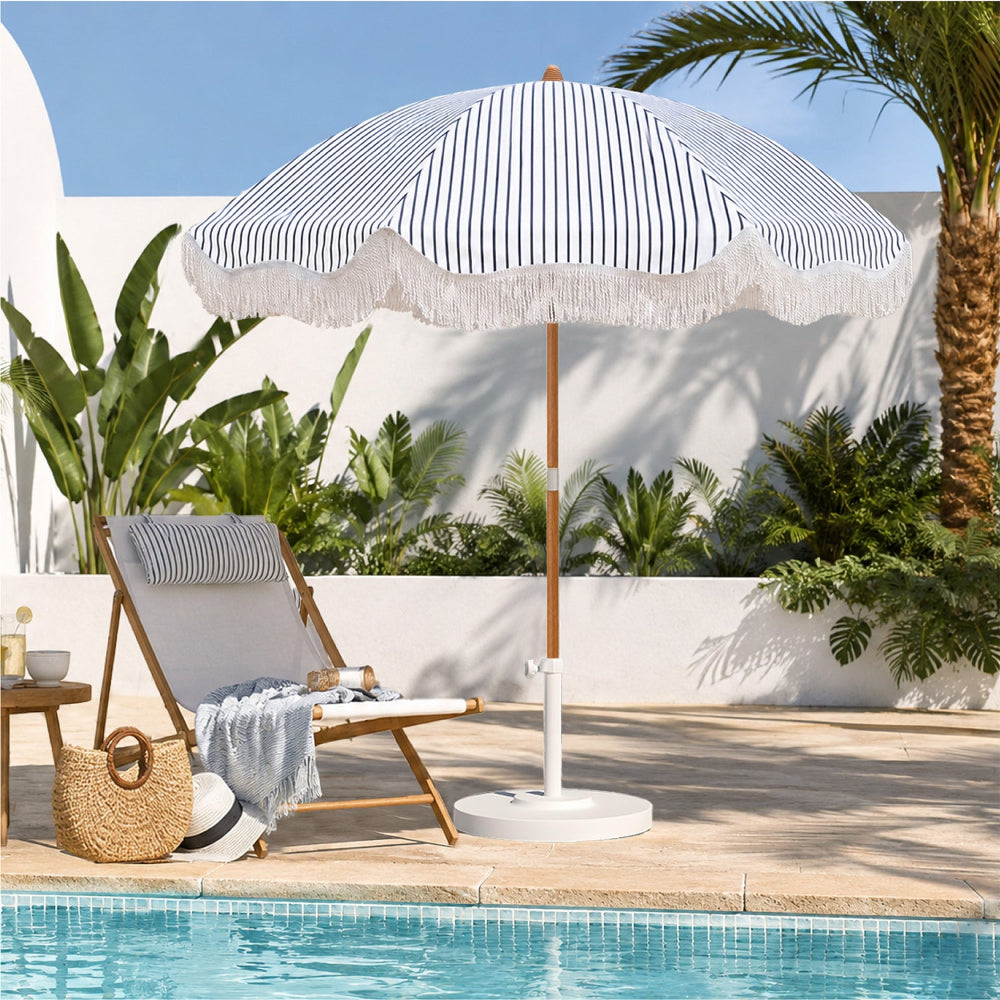 AMMSUN 6.5ft navy blue striped boho patio umbrella with fringe stands beside a pool in a sunny outdoor setting, next to a wooden lounge chair