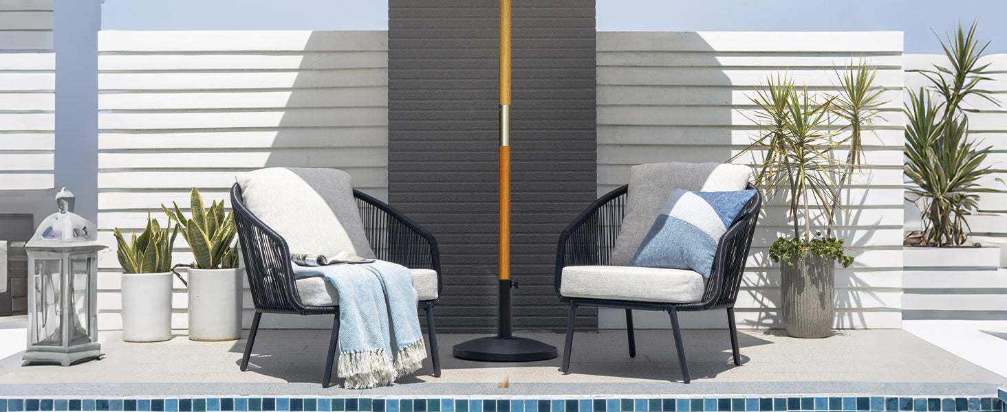Two outdoor chairs with cushions on a patio with plants and a lamp.