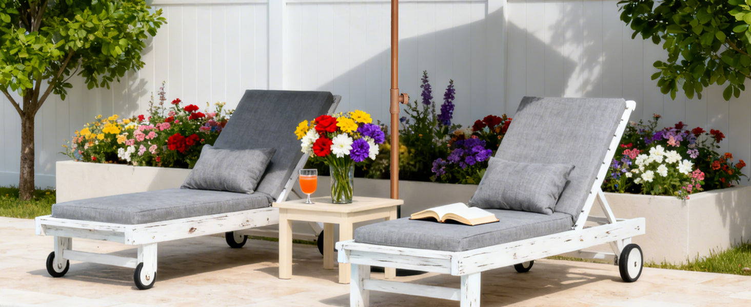 Two white outdoor lounge chairs with gray cushions on a patio with flowers and a table.