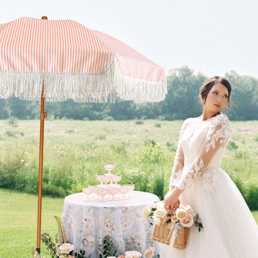The bride stands beside a table adorned with a pink boho umbrella fringe decorative umbrella for outdoor