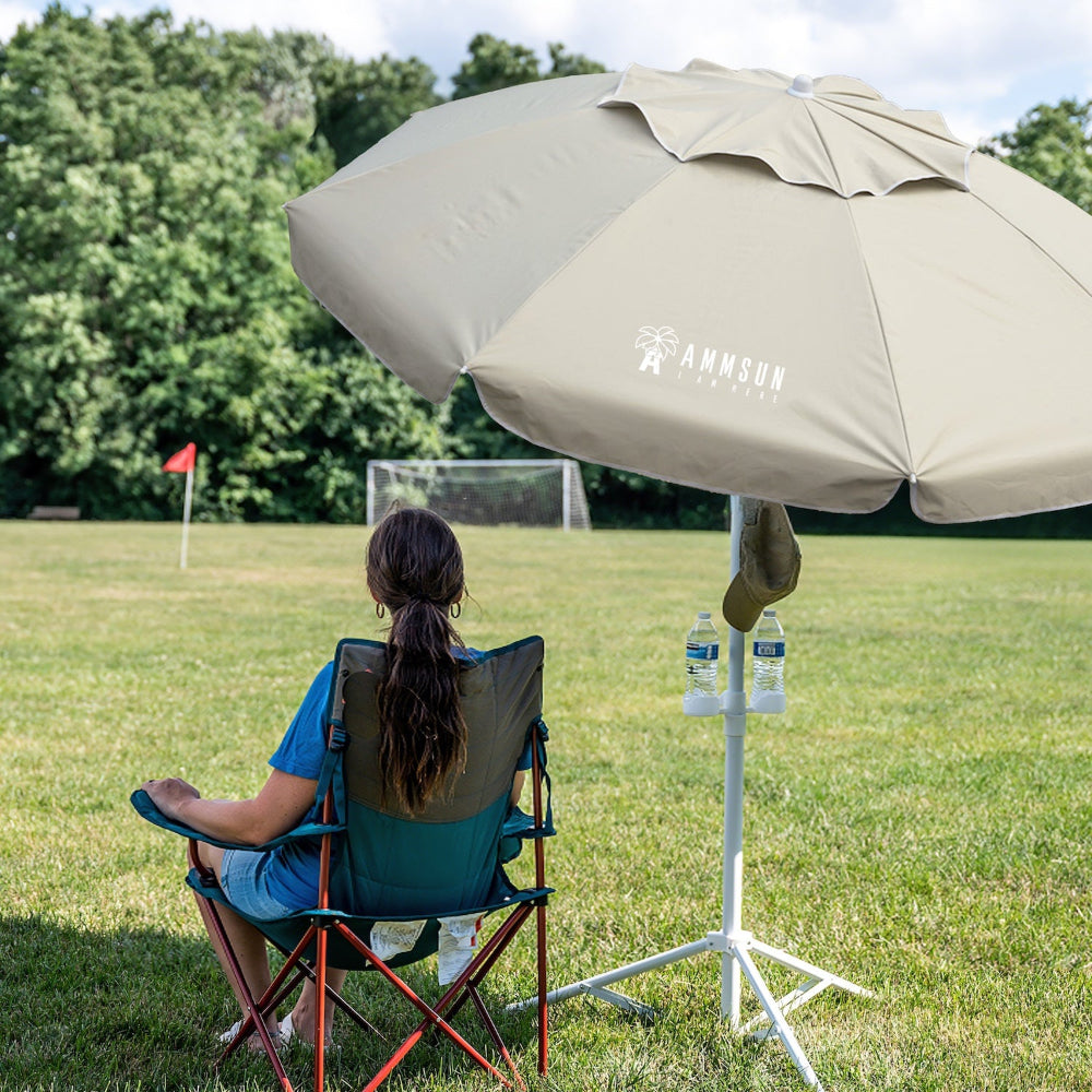 Person sitting under sn AMMSUN beige lightweigt umbrella for outdoor sports umbrella with stand on grass