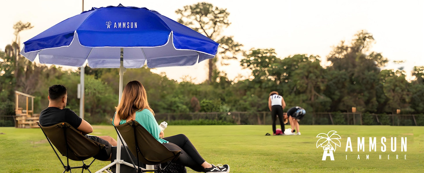 Two people sitting under a large blue Ammsun shade umbrella with stand for sports umbrella on a grass