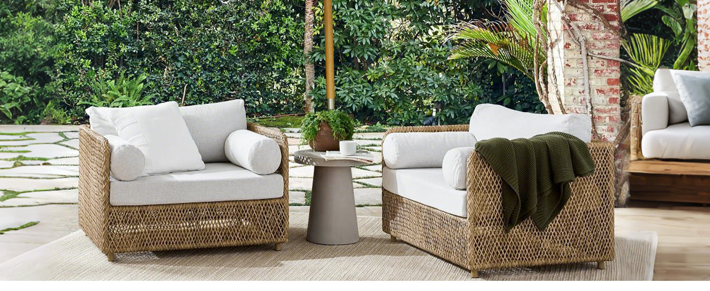 Two wicker chairs and a small table arranged on a cozy patio, surrounded by greenery