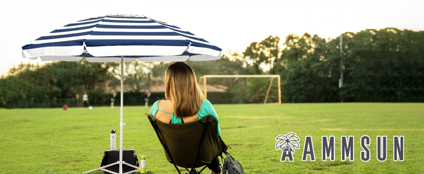 A woman sitting under an AMMSUN 6.5ft blue navy sports umbrella portable umbrella for travel with stand on the football field.