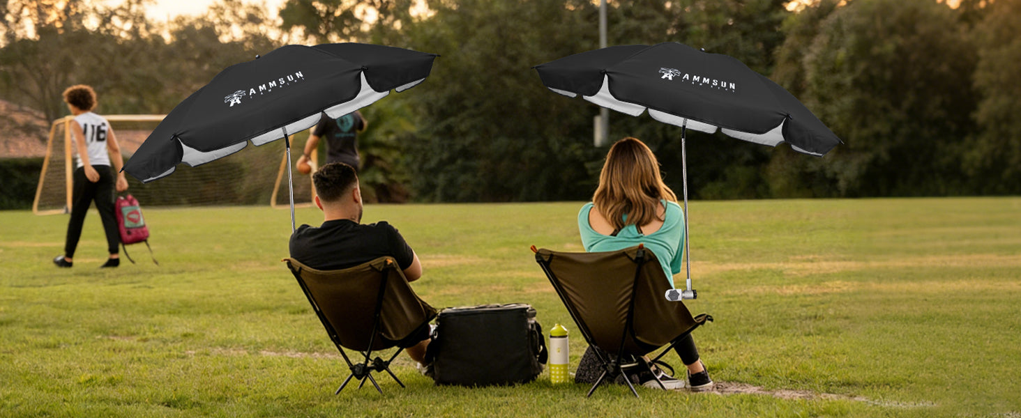 Two people sitting in chairs with AMMSUN black 47inches sport umbrella with clamp are placed on the soccor field