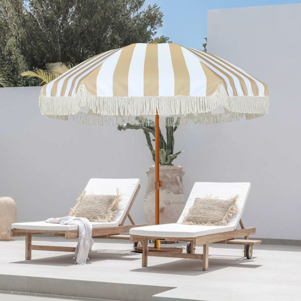 Two wooden lounge chairs with AMMSUN 7ft beige stripes uv umbrellas for sun protection with fringe for beach on sunny day.