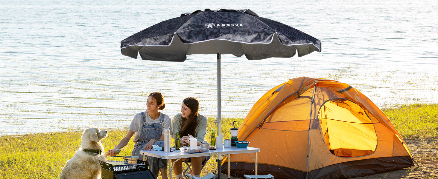 Two women seated under an AMMSUN 6.5ft camouflage beach umbrella heavy duty with a dog beside them