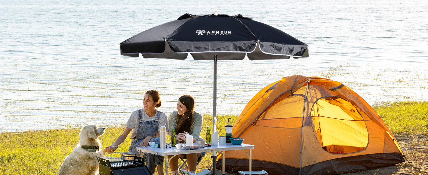 Two women relax under an AMMSUN 6.5ft black portable beach umbrella while a dog sits beside them