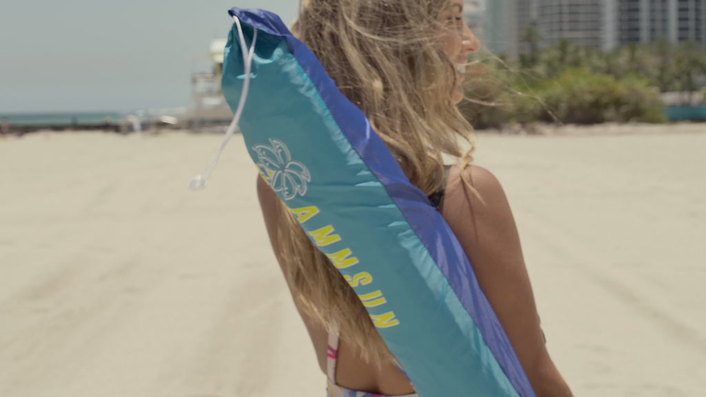 A woman carrying AMMSUN 7.5ft rainbow portable travel beach umbrella with sand anchor to the beach